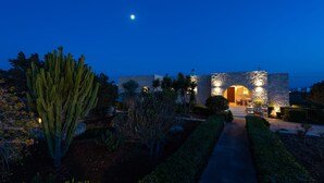 A stone building with an arched entrance, surrounded by cacti and shrubs, under a night sky with a visible moon. - Sun and Salt 3bedroom House (Paros)