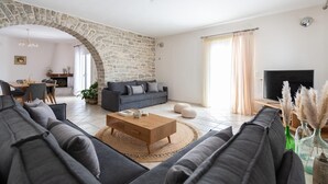 A modern living room with a stone archway, a dark sofa set, a wooden coffee table, and a TV. - Sun and Salt 3bedroom House (Paros)