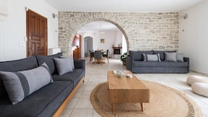 A living room with a stone archway, two sofas, a coffee table, and a dining area in the background. - Sun and Salt 3bedroom House (Paros)