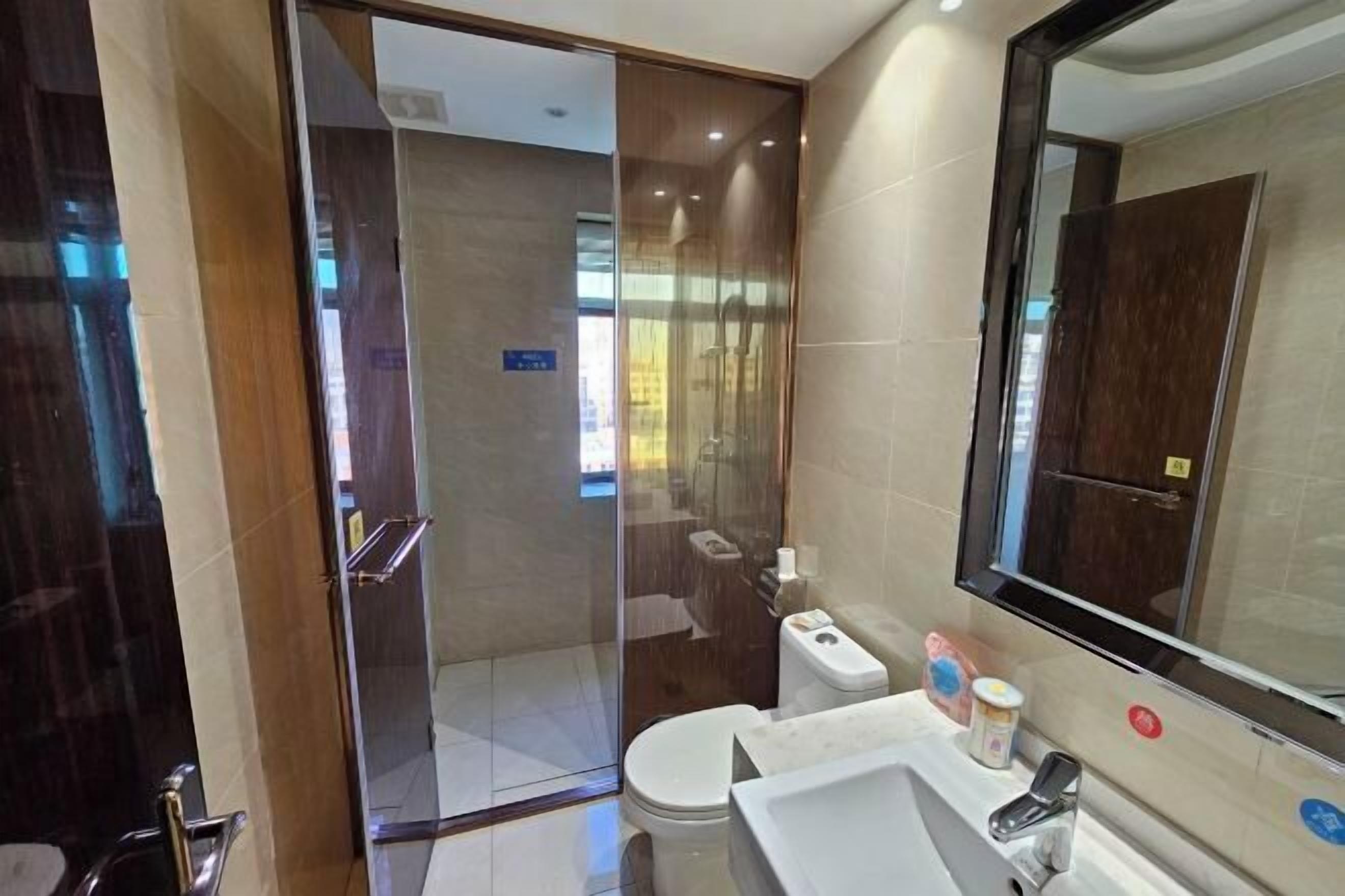 A modern bathroom with a glass shower enclosure, a toilet, a sink, and a large mirror.