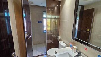 Un baño moderno con cabina de ducha de vidrio, inodoro, lavamanos y un espejo grande.