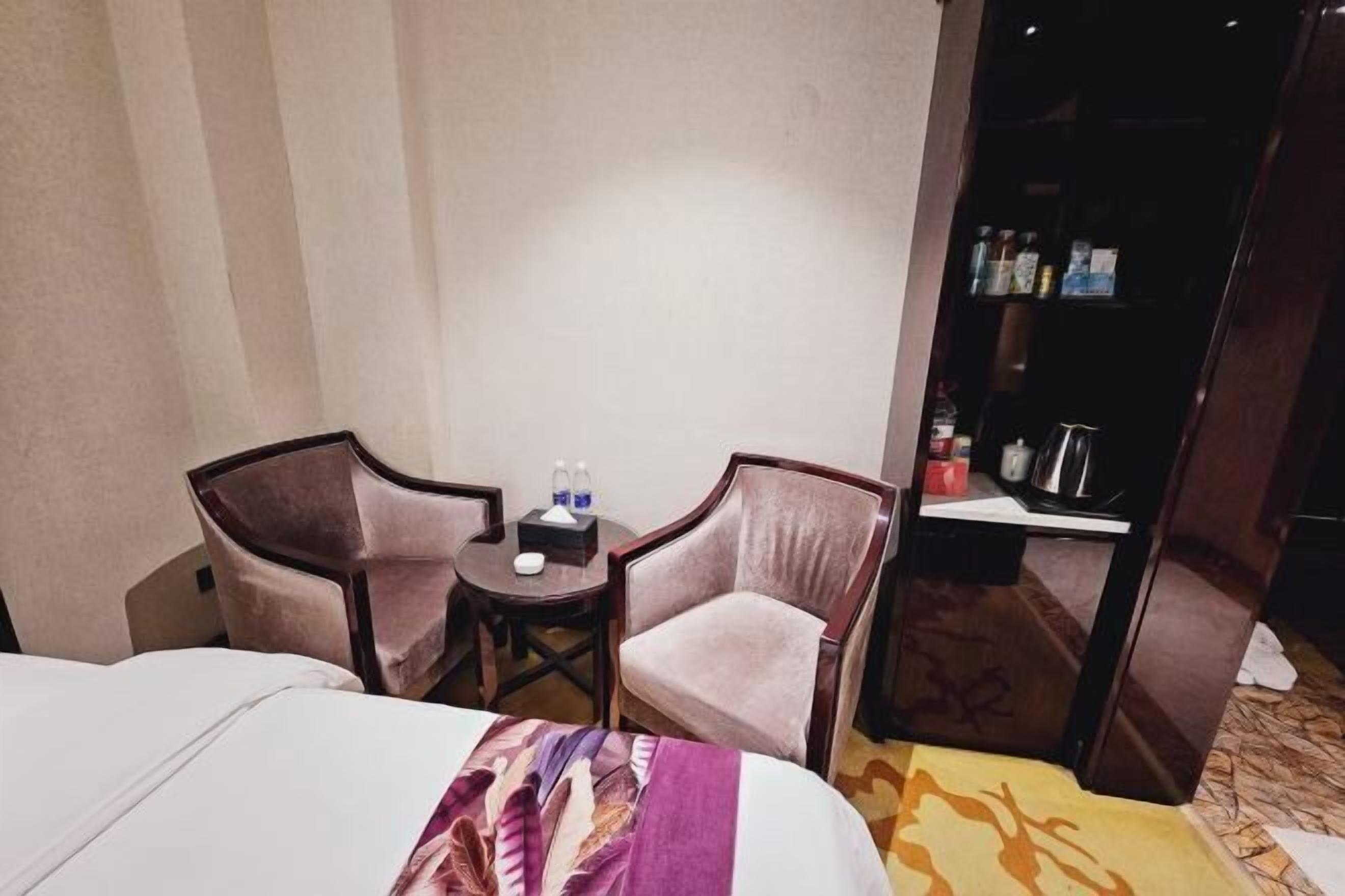 A hotel room with two beds, a small table with chairs, a minibar, and a wardrobe.