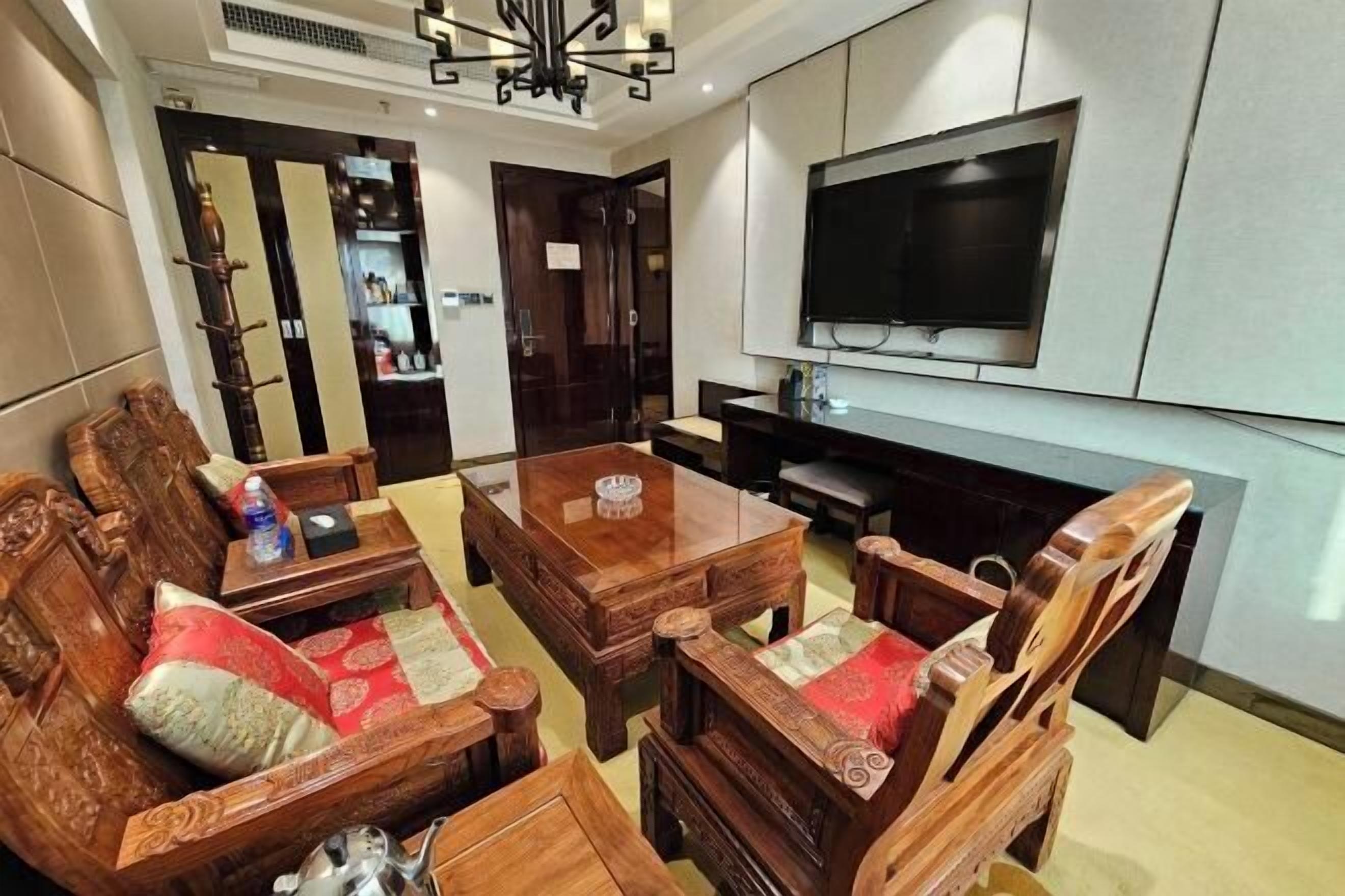 A living room with a wooden sofa set, a coffee table, and a flat-screen TV mounted on the wall.