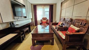 Una sala de estar moderna con un televisor de pantalla plana grande montado en la pared, una mesa de centro de madera, un sofá con cojines estampados y un sillón rojo.