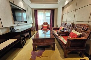 Una sala de estar moderna con un televisor de pantalla plana grande montado en la pared, una mesa de centro de madera, un sofá con cojines estampados y un sillón rojo.