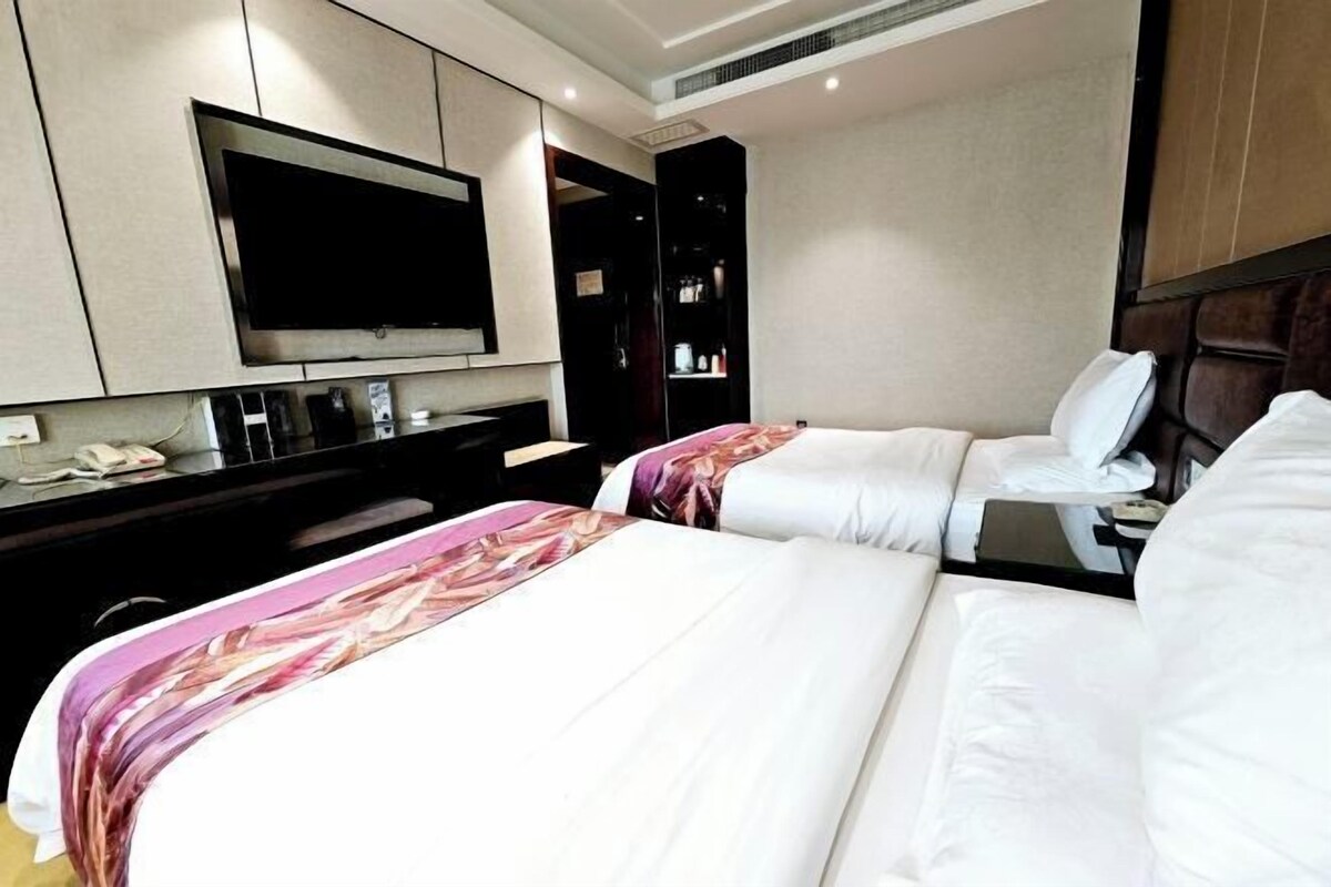Une chambre d’hôtel avec deux lits, un téléviseur à écran plat, un minibar et un bureau avec une chaise.