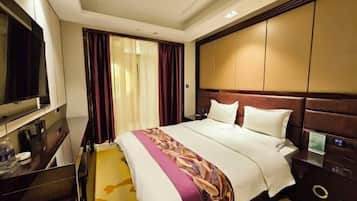 Habitación de hotel con una cama grande, un televisor a la izquierda, un escritorio con una silla y una ventana con cortinas.
