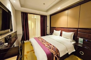 Habitación de hotel con una cama grande, un televisor a la izquierda, un escritorio con una silla y una ventana con cortinas.