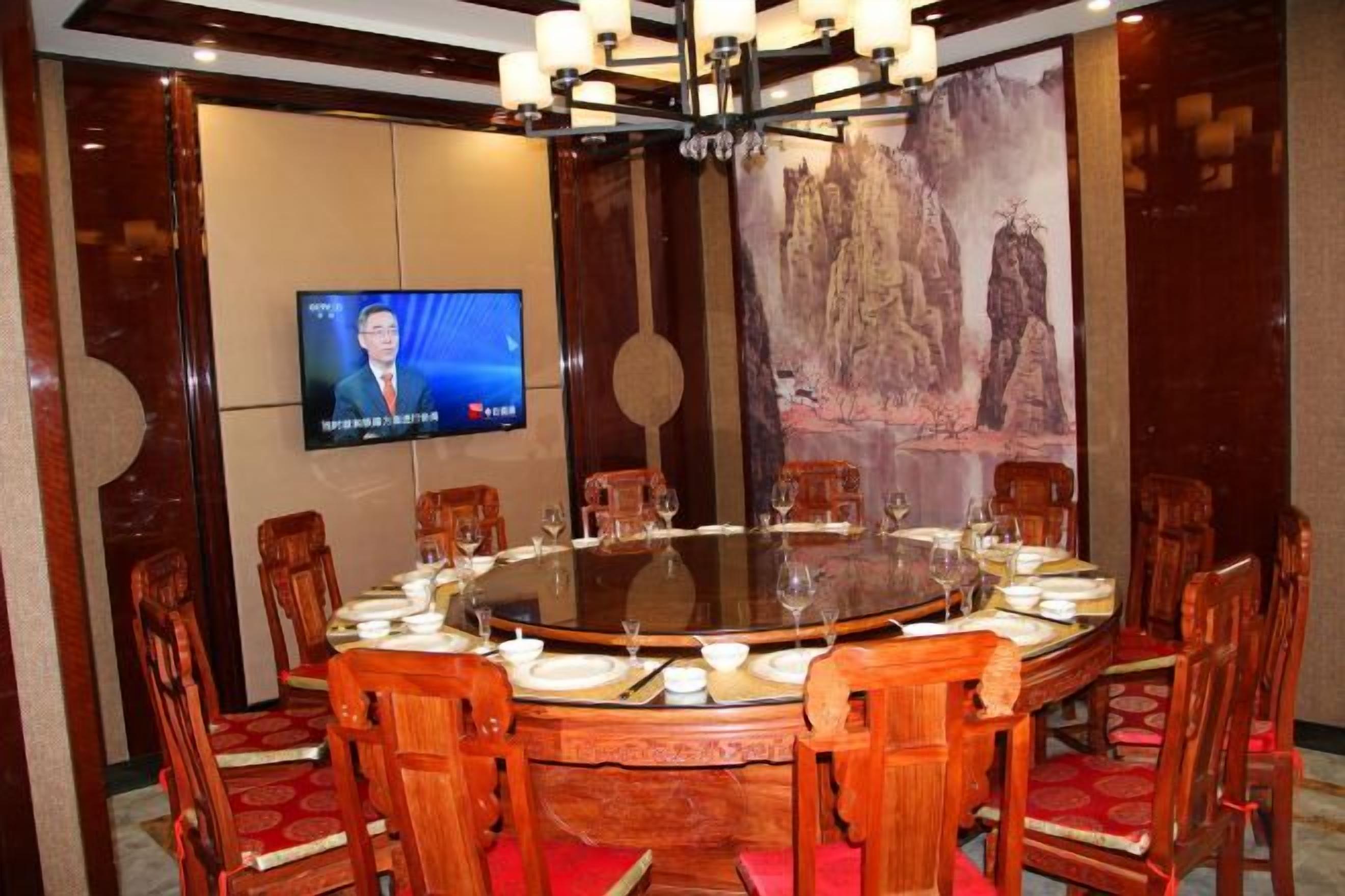 Un salón de conferencias con una mesa redonda, sillas, una pantalla de televisión y un cuadro grande.