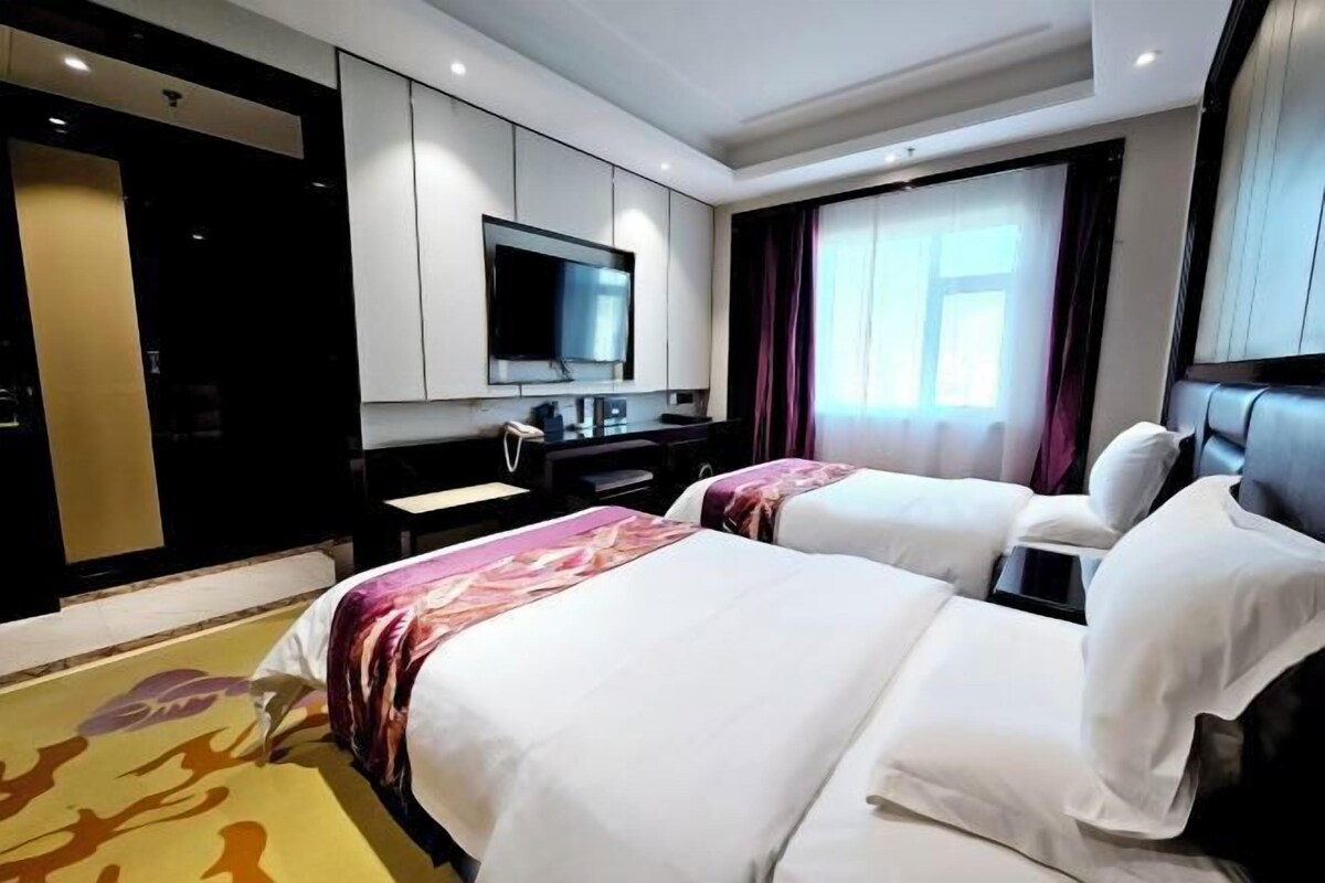 Une chambre d’hôtel avec deux lits, un téléviseur à écran plat fixé au mur, un bureau avec une chaise et une grande fenêtre avec des rideaux.