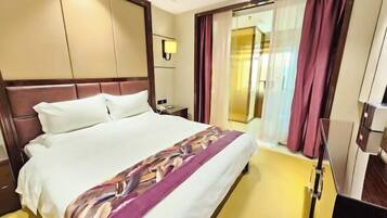 Habitación de hotel con una cama grande, una mesita de noche, una lámpara y vistas al exterior a través de una ventana con cortinas.