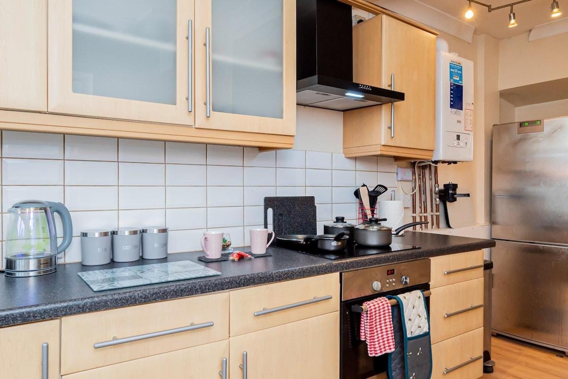 A modern kitchen with light wood cabinets, a stainless steel refrigerator, and a black countertop.