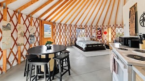 A cozy yurt with a bed, a dining area with a table and chairs, and a kitchen with a stove.
