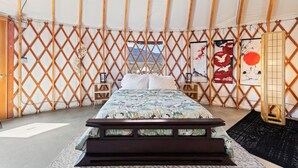 A bed in a tent with a lattice wall, a wooden bench, and artwork on the walls.