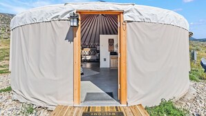 A yurt with a wooden door, a welcome mat, and a view of the interior including a kitchen and a bed.