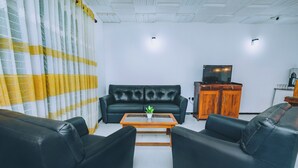 Un salon avec un canapé en cuir noir, une table basse en bois et un téléviseur posé sur un meuble en bois.