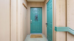 A hallway with a teal door, a doormat, and a wooden handrail.