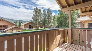 A wooden deck with a railing, overlooking a courtyard with buildings and trees.