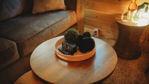 Un tavolo rotondo in legno con un cesto intrecciato contenente una piccola pianta, un oggetto decorativo e un telecomando.