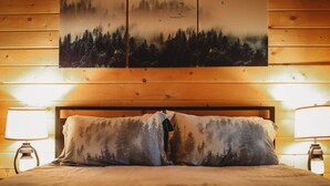 Un letto con due cuscini, una testiera in legno e un quadro appeso al muro raffigurante una scena di bosco.
