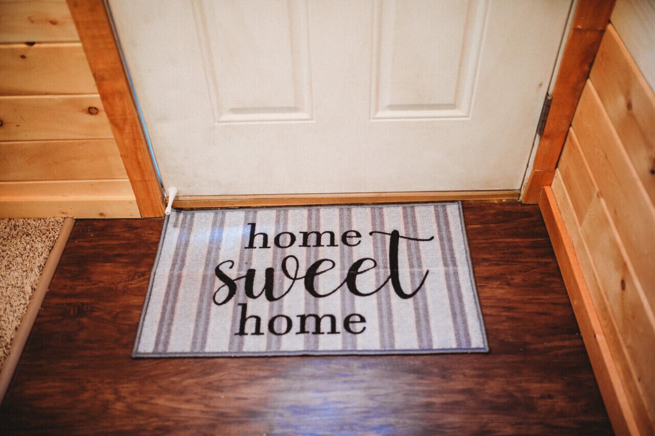 Een deurmat met de tekst 'home sweet home' op een gestreepte ondergrond.