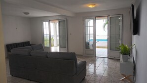 Un salon avec un canapé gris, un téléviseur à écran plat fixé au mur et une plante en pot posée sur une petite table.
