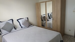 A bedroom with a bed, pillows, a wardrobe, and a mirror. - Vacances L'ouest Reunion (La Possession)