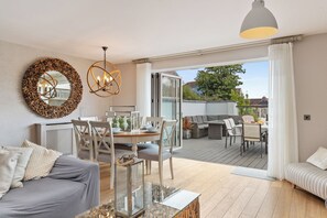 A modern living room with a dining area, a large mirror, and a view to an outdoor deck. - Ger Y Mor - Village Centre with Parking (Saundersfoot)