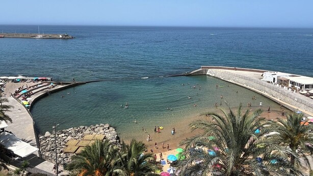 Une plage côtière offrant une vue dégagée sur la mer, un rivage rocheux et une jetée en arrière-plan.