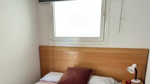 Un lit bien fait, avec une tête de lit en bois, une fenêtre au-dessus et une table de chevet sur laquelle se trouve une lampe.