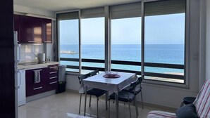 Une cuisine compacte avec un coin repas, de grandes fenêtres donnant sur la mer et un petit canapé.