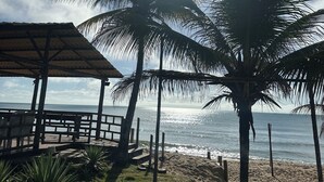 A beach scene with a wooden structure, palm trees, and the ocean. - Hotel Paraiso Tropical (Alcobaca)