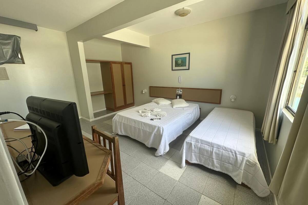 Habitación de hotel con dos camas, un escritorio con silla, televisor y ventana con cortinas.