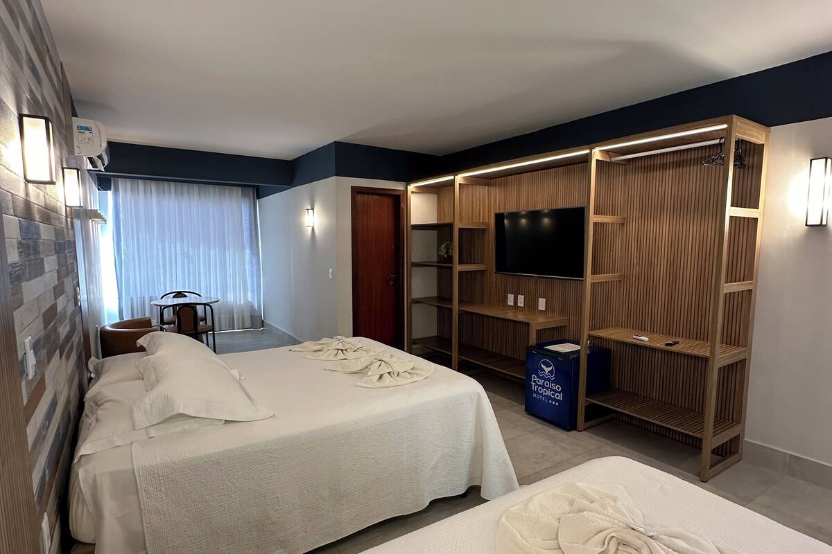 Una habitación de hotel con dos camas, un televisor, un armario y una mesita.