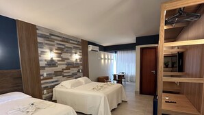 A hotel room with two beds, a wooden wardrobe, a wall-mounted air conditioner, and a small table with a chair. - Hotel Paraiso Tropical (Alcobaca)
