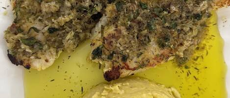 A plate with a fish fillet, a dollop of yellow sauce, and some herbs.