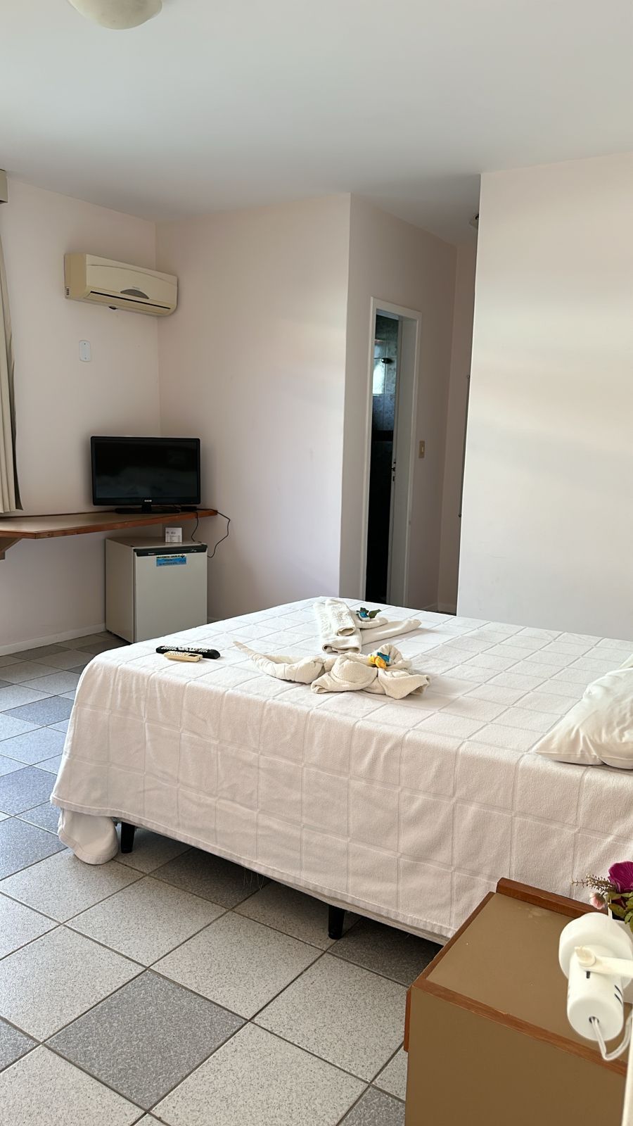 Ein Hotelzimmer mit Bett, Fernseher, kleinem Kühlschrank und einer Tür zu einem Flur.