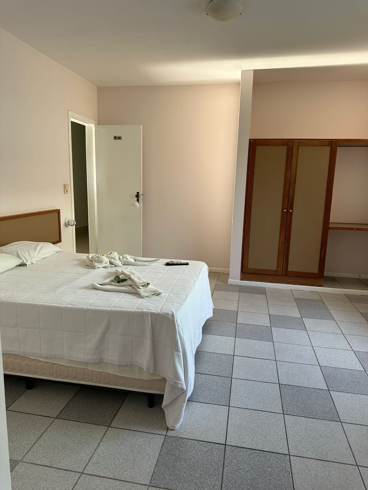 A hotel room with a bed, a wardrobe, and a door leading to another room.