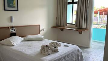 A hotel room with a bed, a bedside phone, a window with curtains, and a view of the outside.
