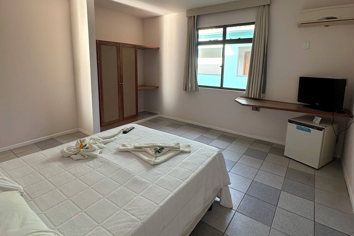 Habitación de hotel con cama, televisor, refrigerador pequeño y ventana con cortinas.