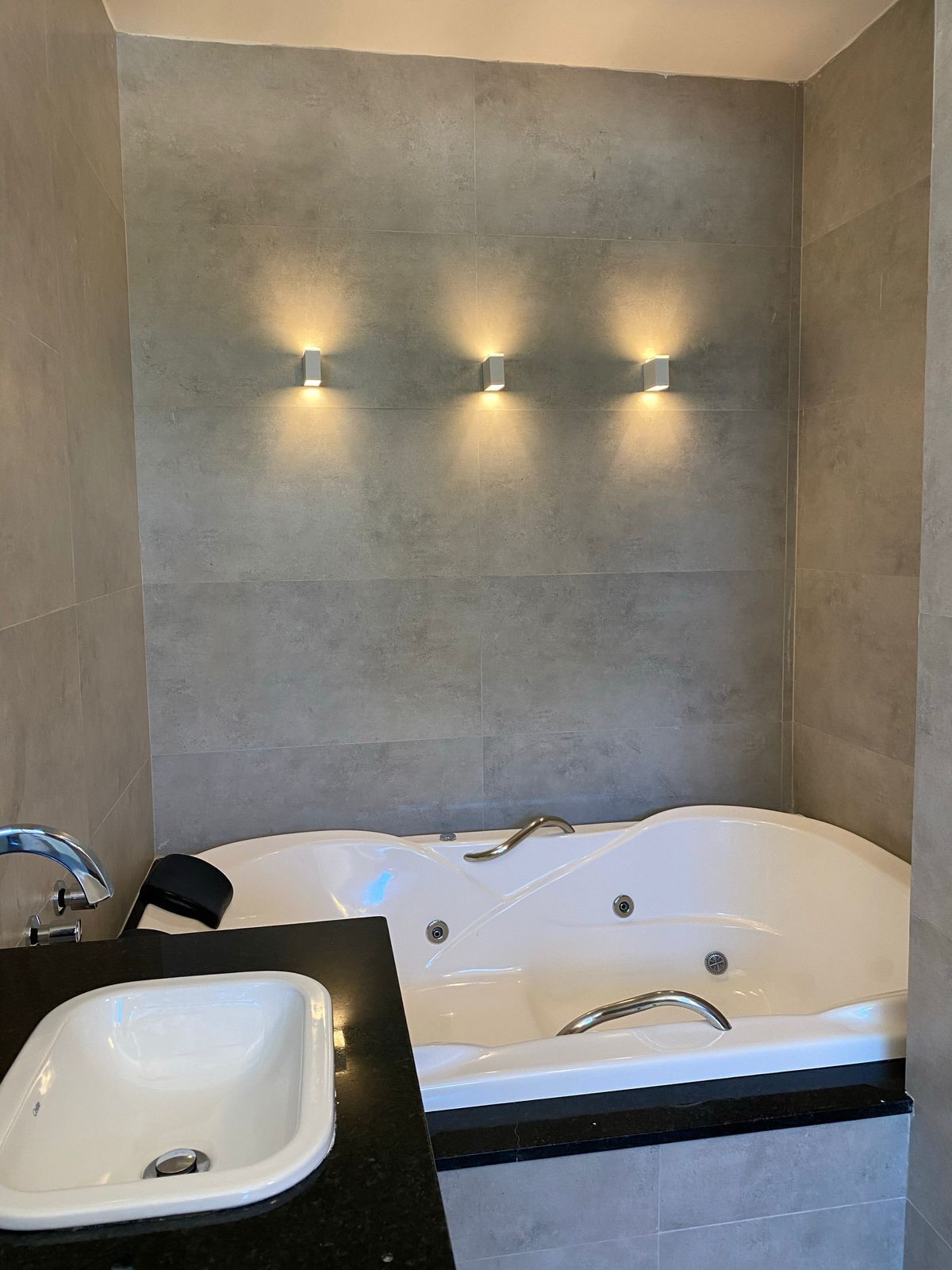 Een moderne badkamer met een vrijstaand bad, een wastafel en drie wandlampen.