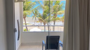 A room with a sliding glass door leading to a balcony with a view of palm trees and a beach. - Hotel Paraiso Tropical (Alcobaca)