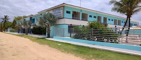 A hotel with a light blue facade, a fenced pool area, and palm trees in the background.
