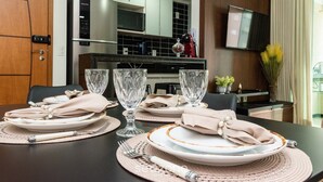Una mesa de comedor dispuesta con platos, vasos y cubiertos, con una cocina al fondo.