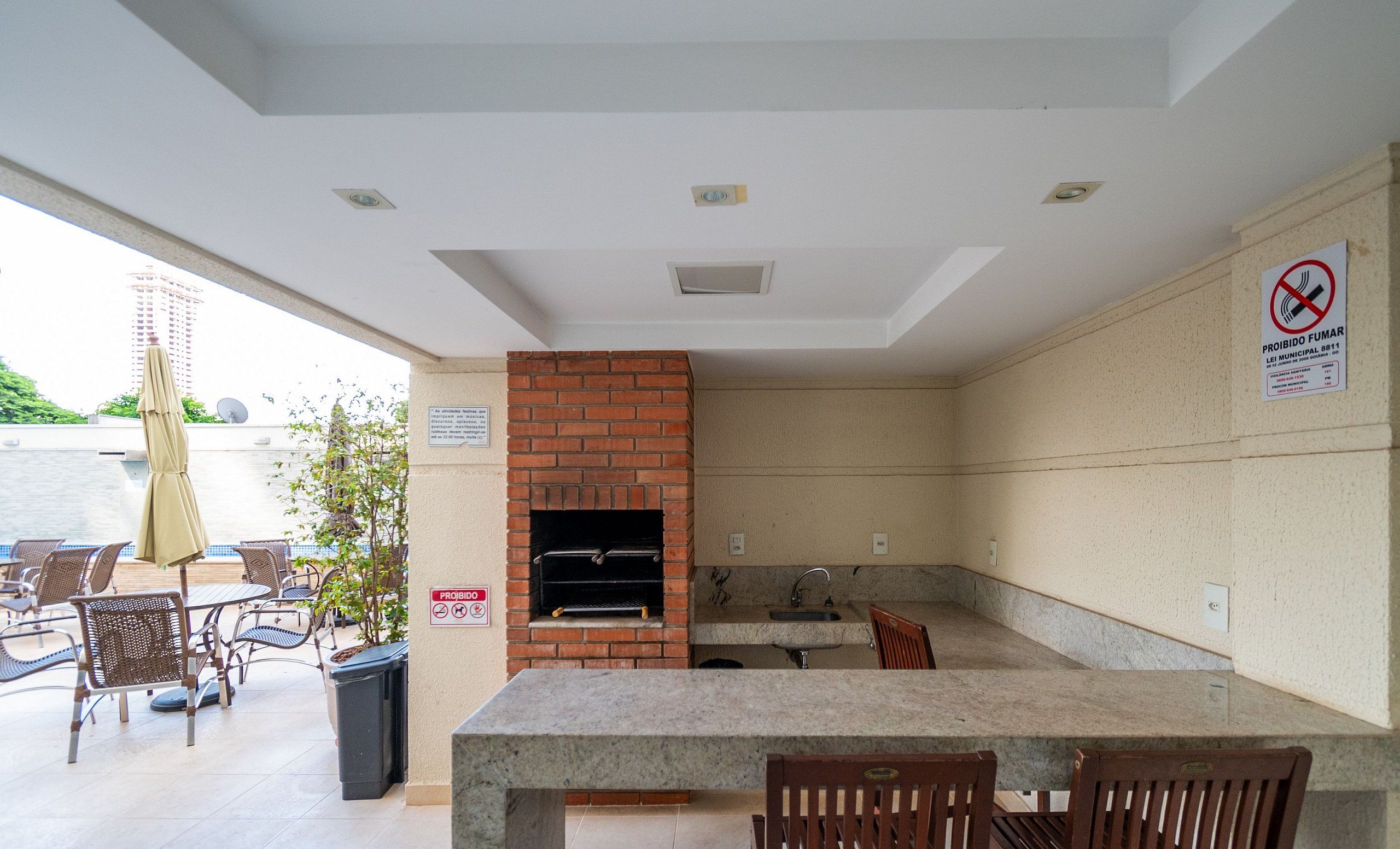 An outdoor patio area with a brick fireplace, a sink, and a table with chairs. There is a sign prohibiting smoking.