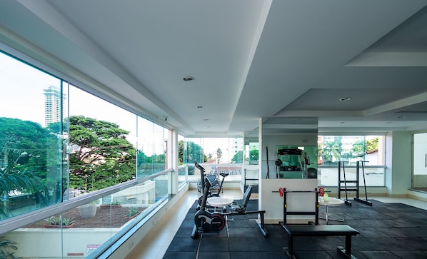 A modern gym with exercise equipment, large windows, and a view of a cityscape. - Ap 2q St Bueno Ed Pontal Premium PPB1206 (Goiânia)