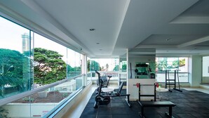 Un gimnasio moderno con equipo de ejercicio, ventanas amplias y vista a un paisaje urbano.