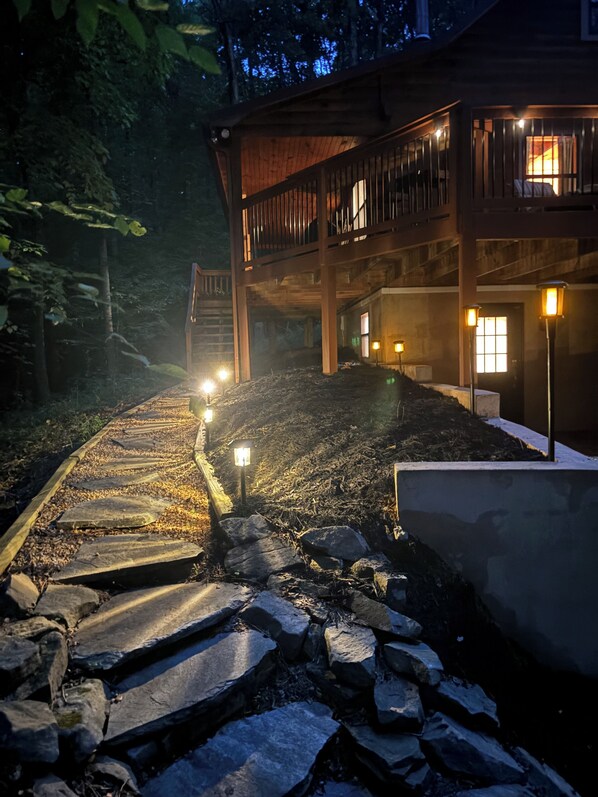 A wooden cabin with a stone pathway leading to the entrance, surrounded by trees. - Rustic Ridge 3-Level Log Cabin, Covered Deck, Hot Tub, Adult Retreat, Kids Loft (Ellijay)