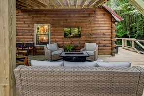 A log cabin with a covered patio area featuring wicker furniture and a fireplace. - Rustic Ridge 3-Level Log Cabin, Covered Deck, Hot Tub, Adult Retreat, Kids Loft (Ellijay)