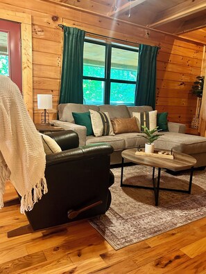 A cozy living room with a leather sofa, a coffee table, and a rug. - Rustic Ridge 3-Level Log Cabin, Covered Deck, Hot Tub, Adult Retreat, Kids Loft (Ellijay)